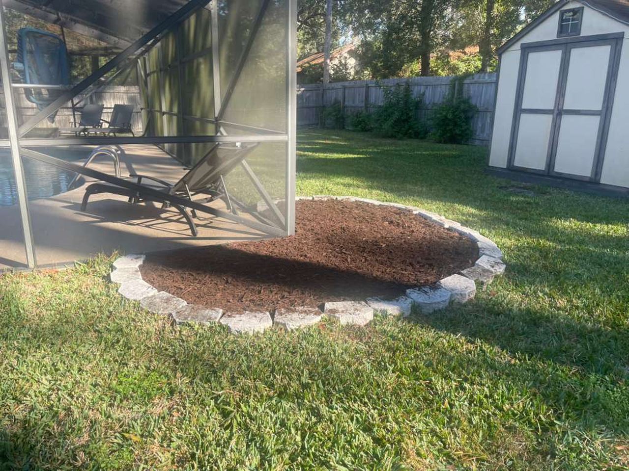After: the same round bed refilled with fresh dark mulch and the stone ring reset.