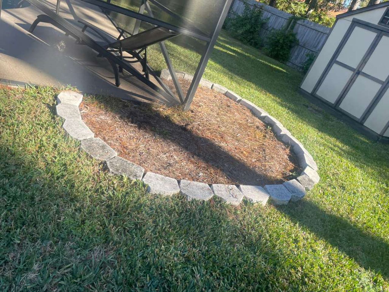 Before: a round garden bed with faded, patchy mulch inside a stone ring.